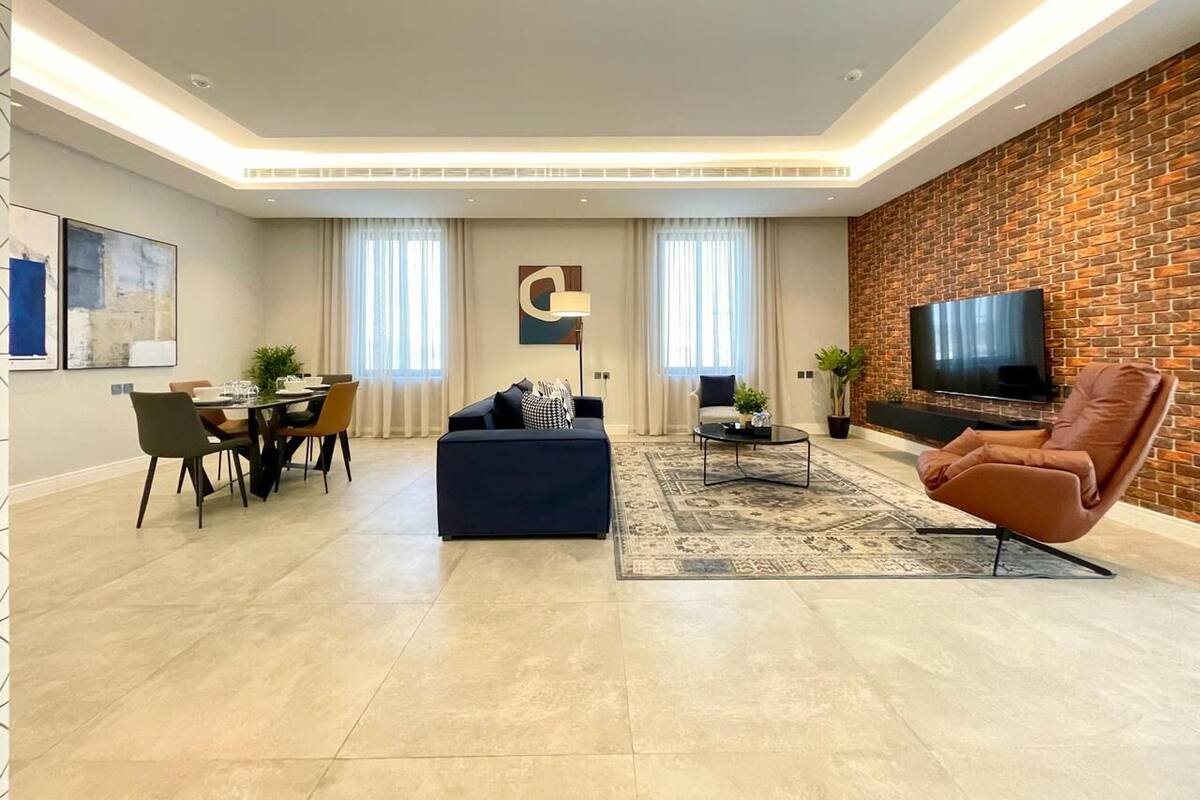 A modern living room with a dining area, a sofa, a coffee table, and a TV against a brick wall.