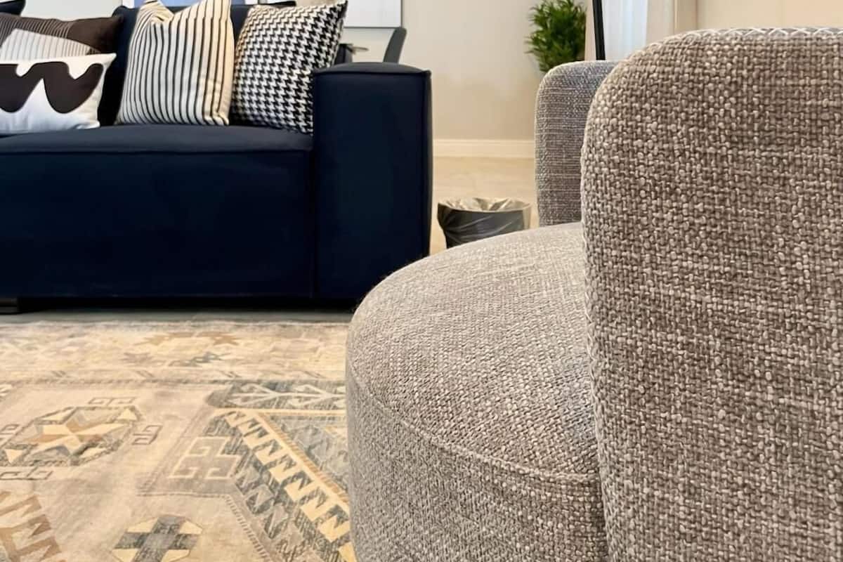 A modern living room with a dark blue sofa, patterned cushions, a textured armchair, a geometric-patterned rug, and abstract wall art.