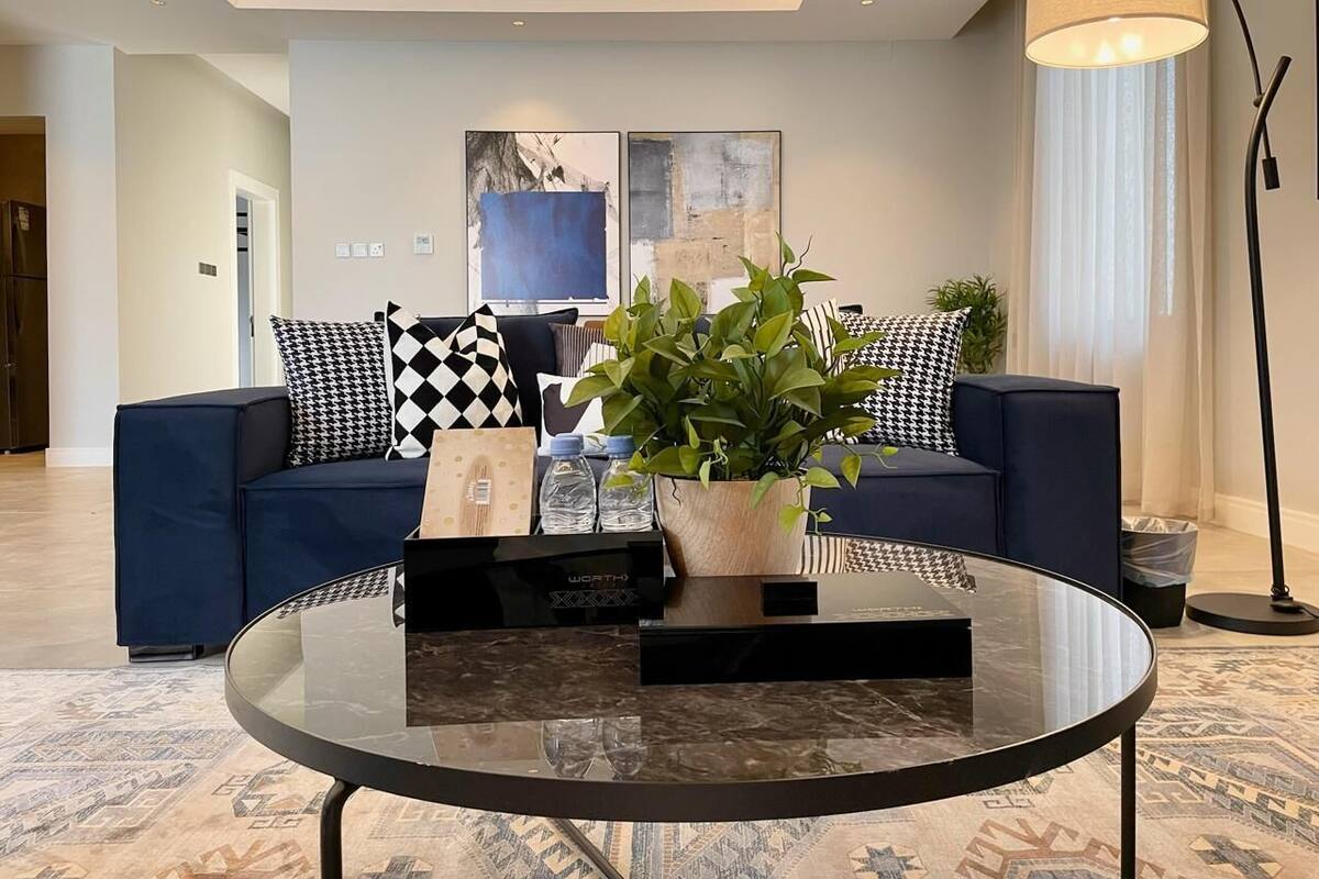 A modern living room with a dark blue sofa, a glass coffee table, and a potted plant.