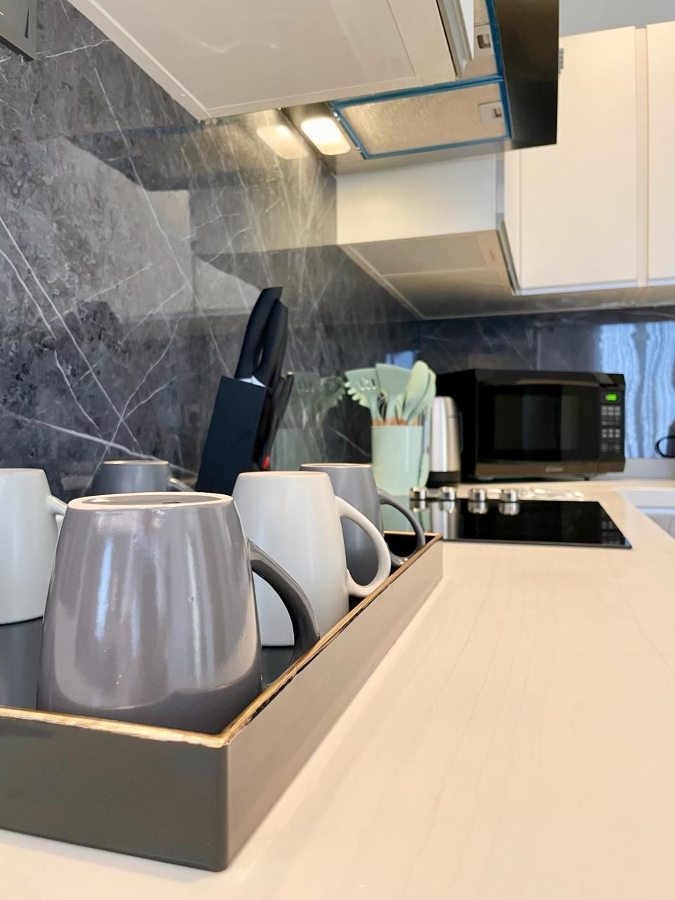 A modern kitchen with a marble backsplash, a coffee station with mugs, a knife block, and a microwave.