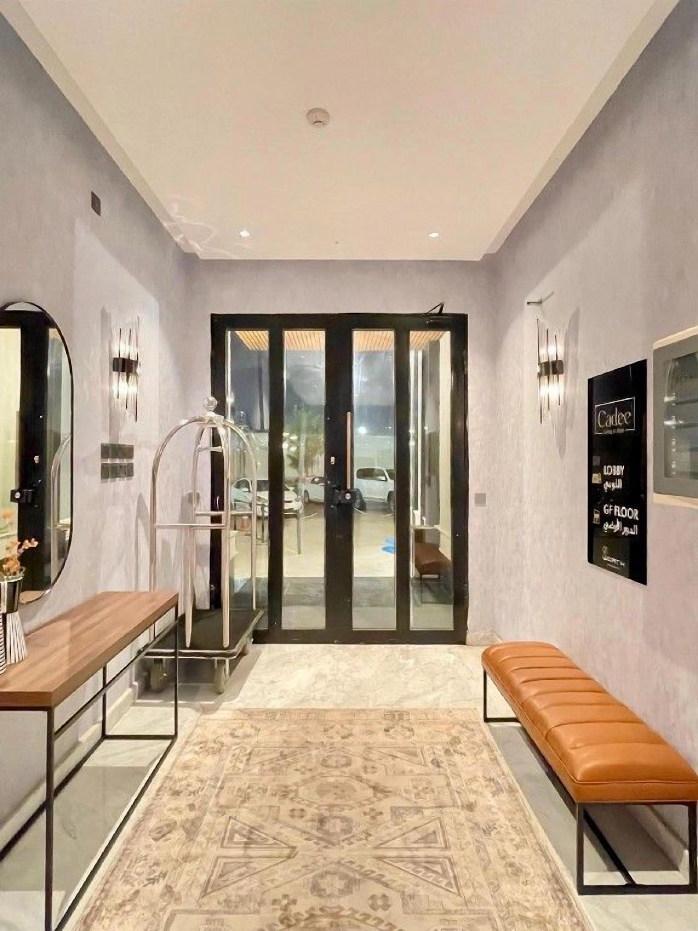 A hotel lobby with a reception desk, a bench, a patterned rug, and a glass door leading outside.