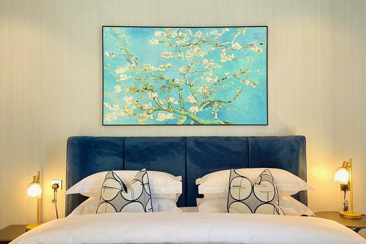 A hotel room with a large bed, two bedside tables with lamps, and a framed artwork of a tree with blossoms on the wall.
