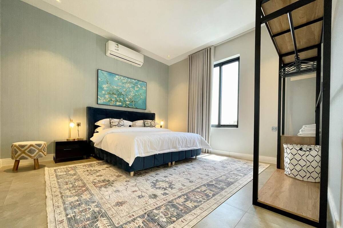 A modern bedroom with a large bed, a decorative rug, a side table, and a window with curtains.