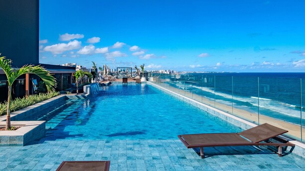 A rooftop pool with clear blue water, a glass railing, and a view of the ocean. - Comfortable Studio with Ocean View in Armação (Salvador)
