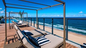 A rooftop lounge with sun loungers and a pool overlooking the ocean. - Comfortable Studio with Ocean View in Armação (Salvador)