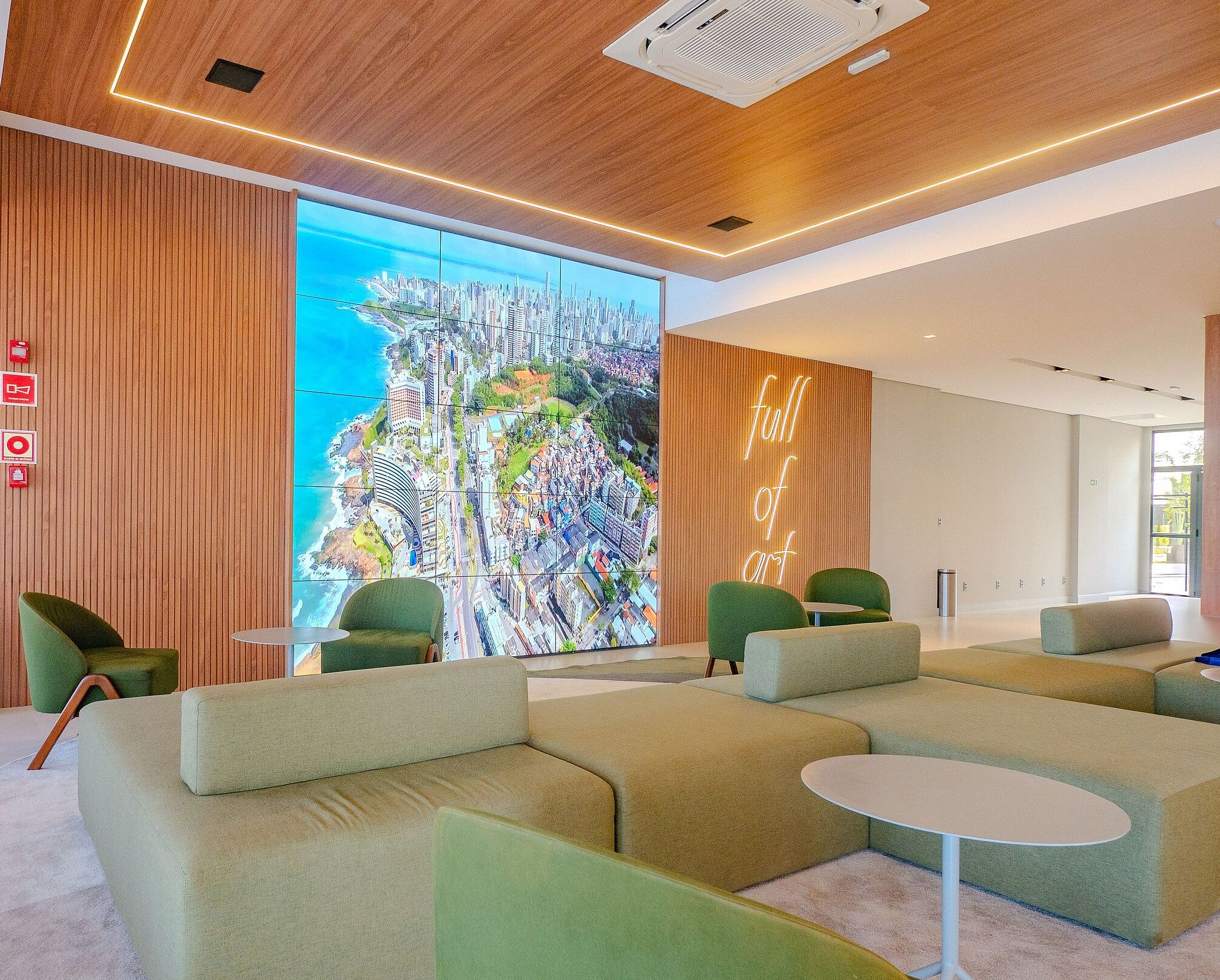 Un hall d’entrée moderne avec des sièges verts, une grande fresque représentant un paysage urbain et une pancarte indiquant « un lieu dédié à l’art ».