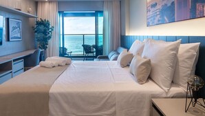 A modern hotel room with a large bed, a desk, and a view of the sea. - Comfortable Studio with Ocean View in Armação (Salvador)