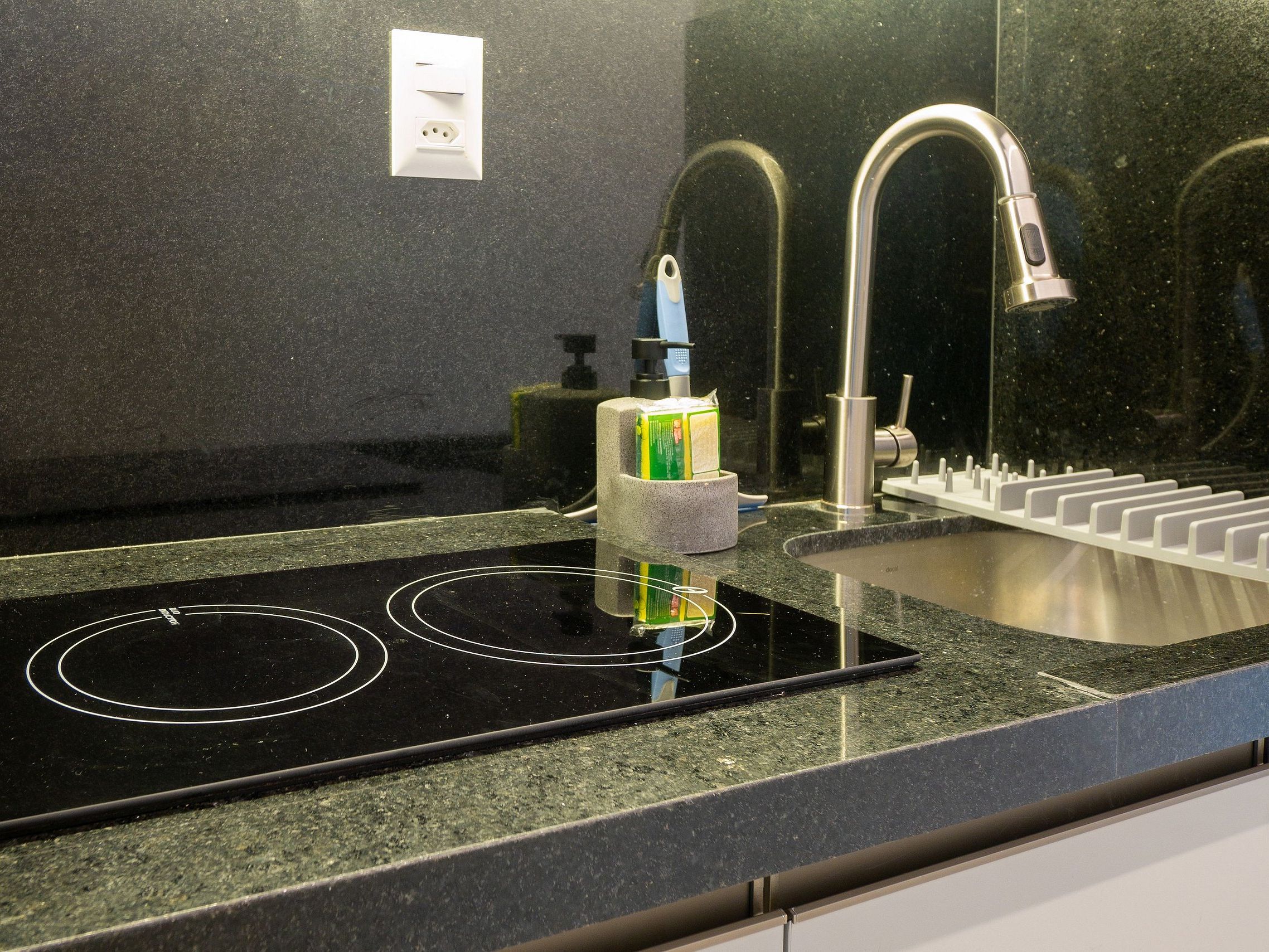 A kitchen with a black induction cooktop, a stainless steel sink, and a granite countertop.