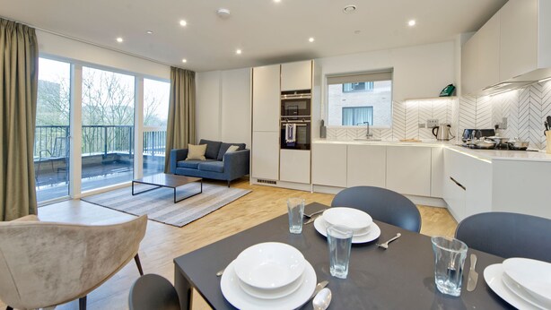 A modern kitchen with white cabinets, a built-in oven, and a herringbone-patterned backsplash. - Modern Two-bedroom Haven in Colindale (London)