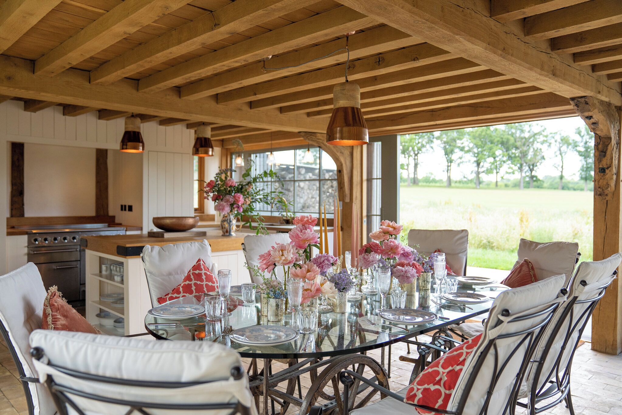Un espace de restauration en plein air avec une table en verre prévue pour six personnes, entourée de chaises en osier dotées de coussins.