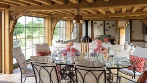 A dining area with a wooden ceiling, large windows, and a table set for four with floral centerpieces. - Wilderness Reserve - Cartshed (Halesworth)