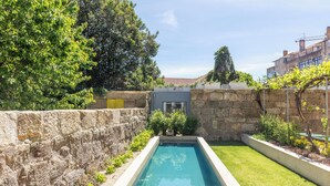 Une piscine rectangulaire, avec un mur en pierre d’un côté et une zone herbeuse de l’autre.