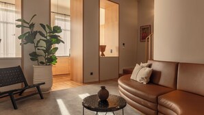 Un salon avec un canapé en cuir marron, un banc en osier noir, une plante en pot et une petite table ronde sur laquelle est posé un vase.