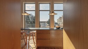 Une cuisine moderne dotée d’une grande fenêtre, de meubles en bois et de deux suspensions lumineuses.