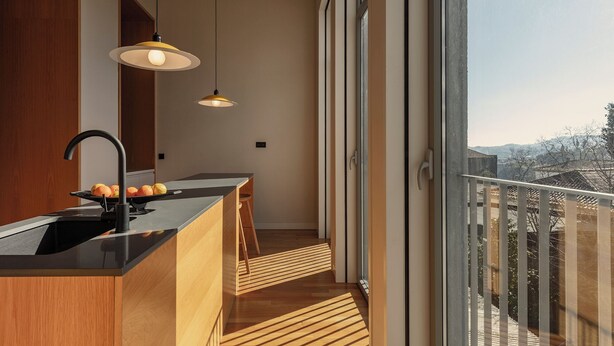 Une cuisine moderne avec un plan de travail noir, des meubles en bois et une grande fenêtre donnant sur un balcon.