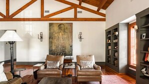 A spacious living room with high ceilings and exposed beams, featuring two leather armchairs, a coffee table, and a large abstract painting on the wall. - Charleston Loft | Exclusive Party-Friendly Rental (Charleston)