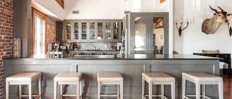 A modern kitchen with a central island, bar stools, and a rustic brick wall.