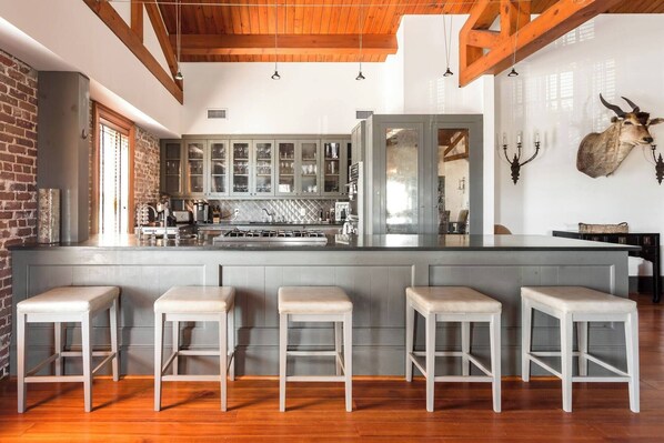 A modern kitchen with a central island, bar stools, and a rustic brick wall.