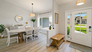 A spacious dining area with a white table and chairs, a wooden bench, and a view of a residential street through a door. - Dockside Dreams - Summer Pool and Canal Retreat! (Palm Coast)