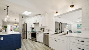 A modern kitchen with white cabinetry, stainless steel appliances, and a blue accent piece. - Dockside Dreams - Summer Pool and Canal Retreat! (Palm Coast)