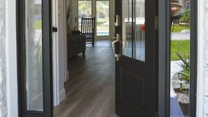 A black-framed door with a welcome mat and a view into a living room with a sofa and a dining area. - Dockside Dreams - Summer Pool and Canal Retreat! (Palm Coast)