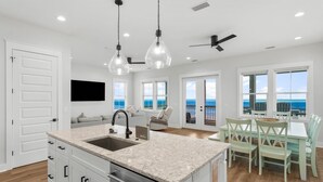 A modern kitchen with a large island, a dining area with a view, and a ceiling fan. - Beach House - Sand Castle Hideaway (Port St. Joe)
