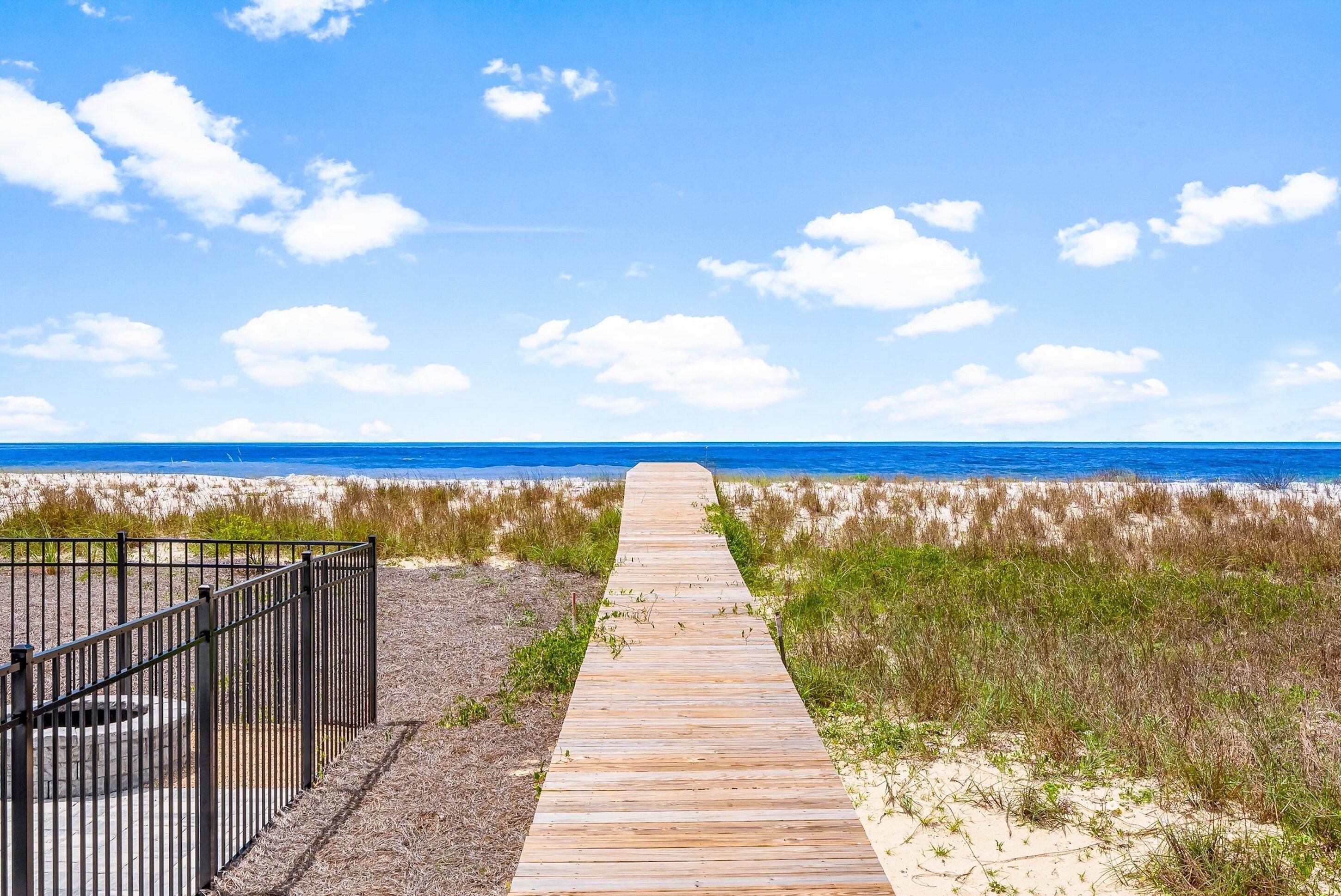 Une promenade en bois menant à une plage, avec une clôture métallique d’un côté.