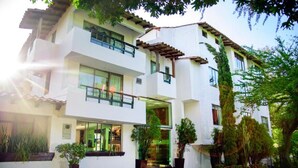 Un edificio de dos pisos con fachada blanca, ventanas grandes y un porche cubierto.