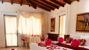 Una habitación de hotel con una cama, una mesa con un letrero que dice 'Love' y globos rojos esparcidos.