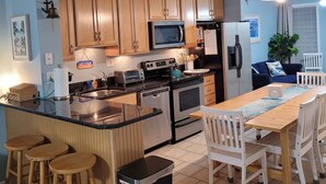 Une cuisine moderne avec des meubles en bois, un îlot central doté de tabourets, un four à micro-ondes, une cuisinière et un réfrigérateur.