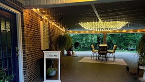 A covered patio area with a brick wall, a welcome sign, outdoor seating with yellow chairs, and string lights. - Spacious 1-bedroom guesthouse in lovely Wiggins with WiFi, AC (Wiggins)