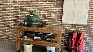 A wooden cart with a green barbecue grill, a white bucket, and red bags of charcoal against a brick wall. - Spacious 1-bedroom guesthouse in lovely Wiggins with WiFi, AC (Wiggins)