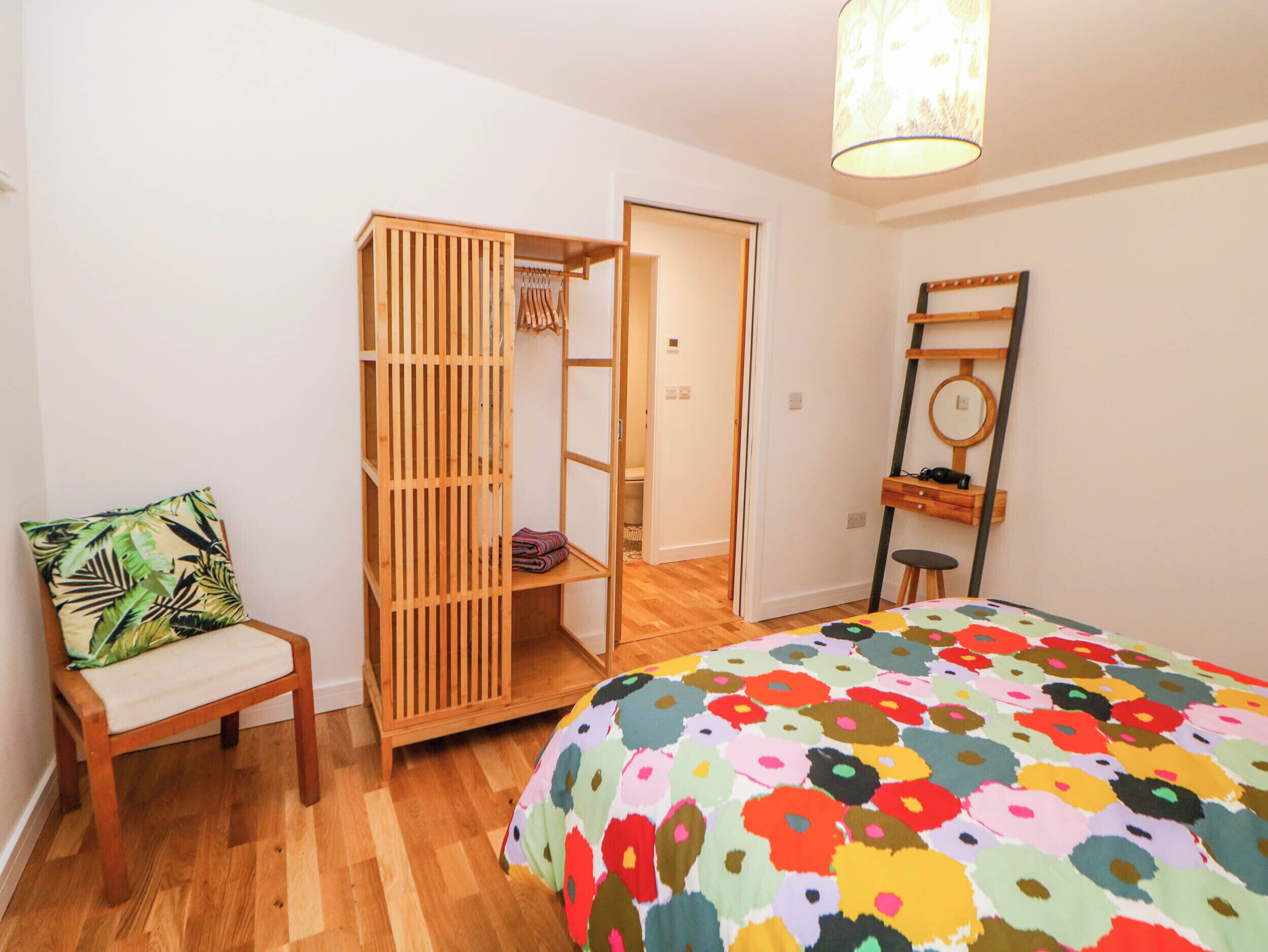Ein Schlafzimmer mit einem Bett, einem Holzschrank, einem Stuhl und einem Schreibtisch mit Spiegel.