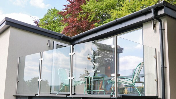 A modern balcony with glass panels, metal railings, and a view of the surrounding area. - Yew Tree Cottage (Matlock)