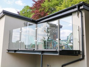 A modern balcony with glass panels, metal railings, and a view of the surrounding area. - Yew Tree Cottage (Matlock)