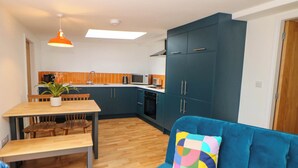 A compact living space with a dining area, kitchenette, and a sofa with a colorful pillow. - Yew Tree Cottage (Matlock)