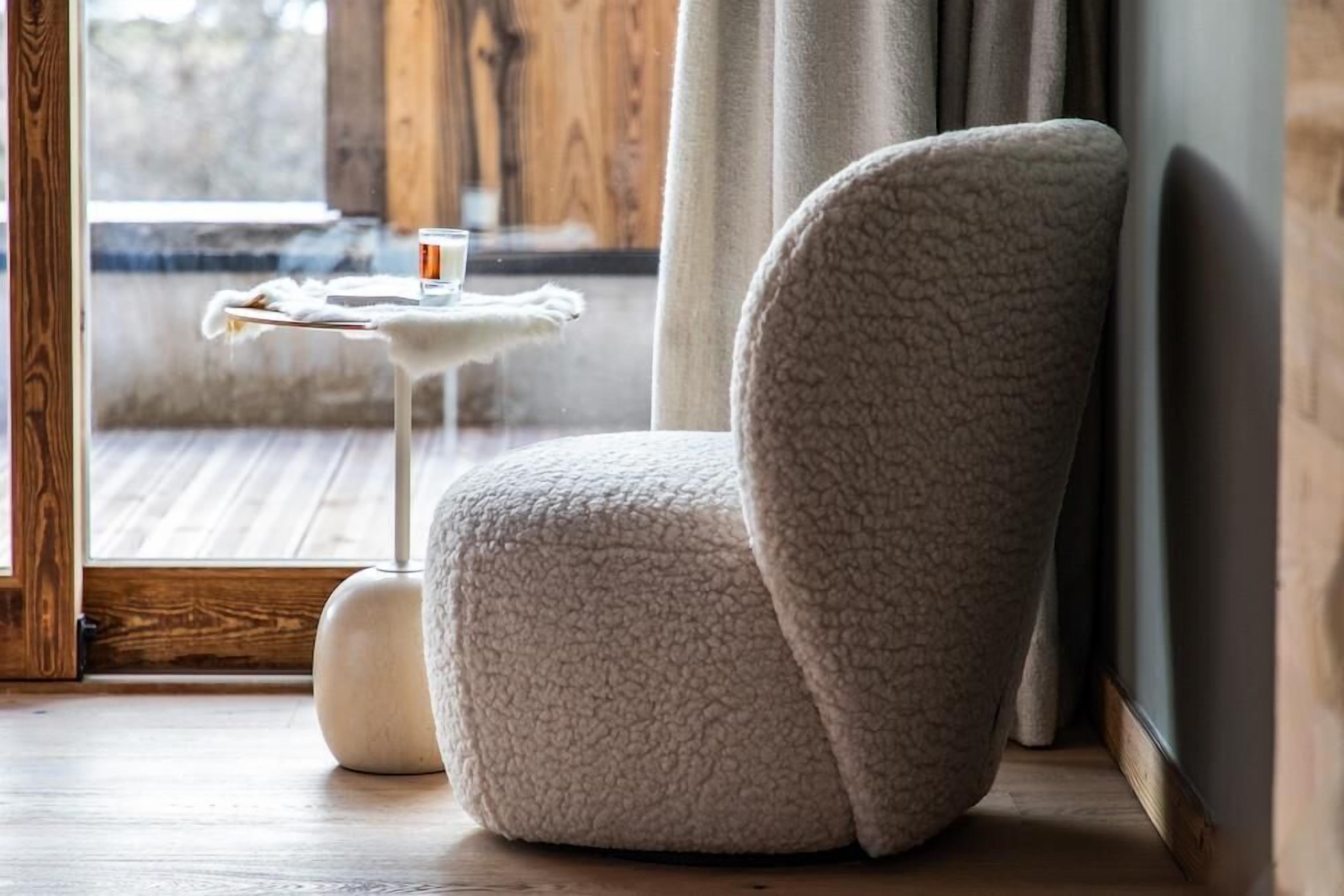 Ein gemütliches Zimmer mit einem bequemen, strukturierten Sessel, einem kleinen runden Tisch mit einem Glas und einem Holzboden.