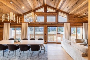 Una habitación amplia con techo de madera, ventanas grandes, una mesa de comedor con sillas y un sofá.