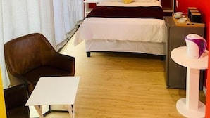 Ein Hotelzimmer mit einem großen Bett, einem Sessel, einem kleinen Tisch und einem Spiegel.