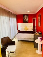 Una habitación de hotel con una cama grande, una silla, una mesita y un espejo.