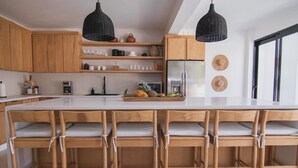 Eine moderne Küche mit Holzausstattung, einer großen Kücheninsel mit Barhocker, schwarzen Pendelleuchten und einem Kühlschrank.