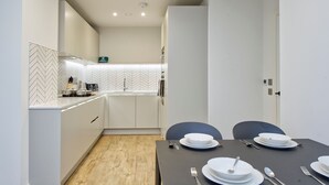 Een moderne keuken met witte kastjes, een backsplash van visgraatmozaïek en een eethoek met een donkere tafel voor vier personen.