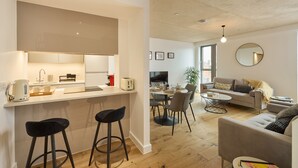 Un appartamento moderno con cucina, zona pranzo e soggiorno. Dispone di uno sgabello da bar, un tavolo da pranzo e un divano.