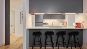 Una cocina moderna con encimera blanca, armarios grises y una cafetera roja.