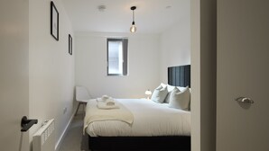 Un dormitorio con cama, lámpara de noche y ventana.