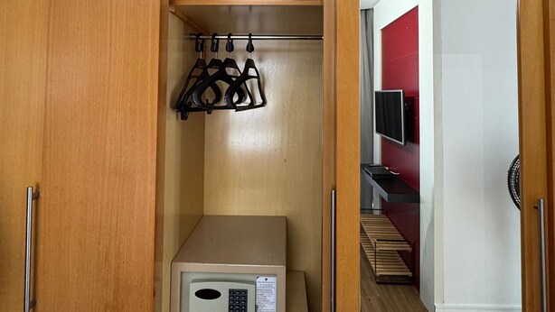 Une petite pièce comprenant une armoire en bois, un four à micro-ondes et une étagère où sont suspendus des vêtements.