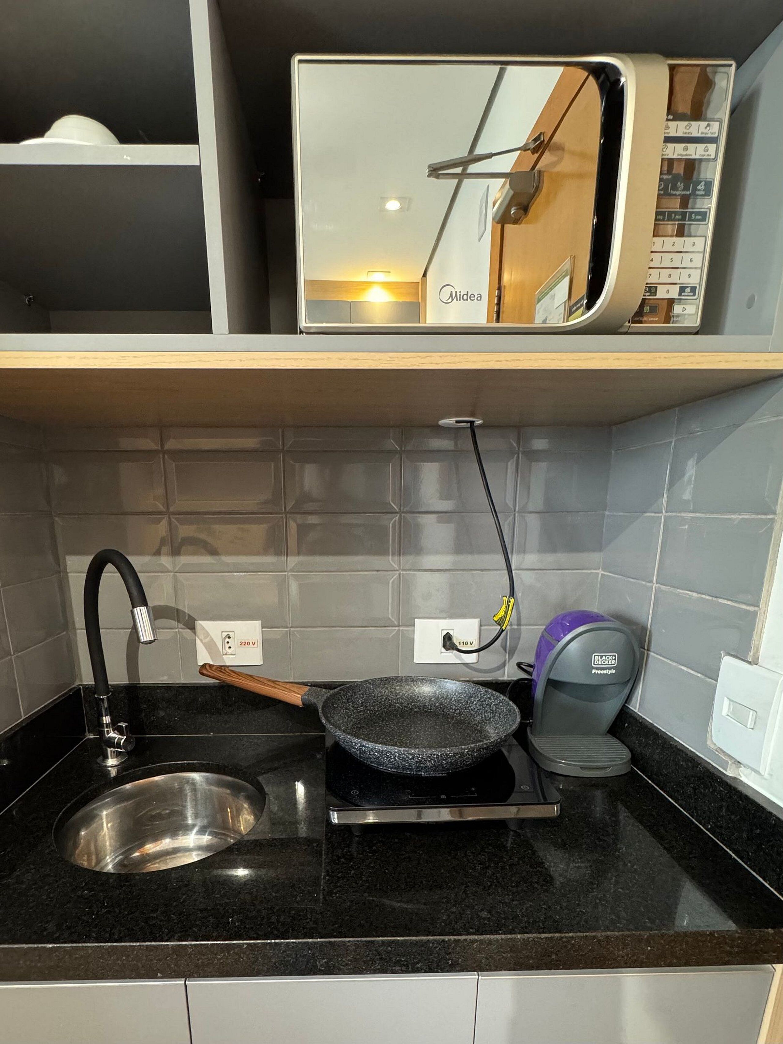 Une cuisine dotée d’un plan de travail noir, d’un évier en acier inoxydable, d’une poêle, d’un four à micro-ondes et d’une multiprise Black & Decker.