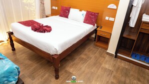 A hotel room with a wooden bed, white bedding, and a red decorative item. There is a wooden nightstand with a remote control, a wooden wardrobe, and a shoe rack with blue shoes. - LOISOI RESORT (Thungari)