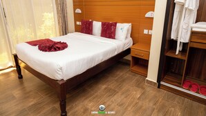 A neatly made bed with white linens and a red decorative item, a wooden headboard, a nightstand with a lamp, and a wooden wardrobe with a mirror and a shoe rack. - LOISOI RESORT (Thungari)