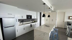 A modern kitchen with white cabinets, a stainless steel refrigerator, a black microwave, and a marble island with stools. - APARTAMENTO VISTA MARE 9-202 (Samana)